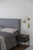Sypialnia z szarym tapicerowanym łóżkiem oraz białą boazerią na ścianie