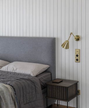 Sypialnia z szarym tapicerowanym łóżkiem oraz białą boazerią na ścianie