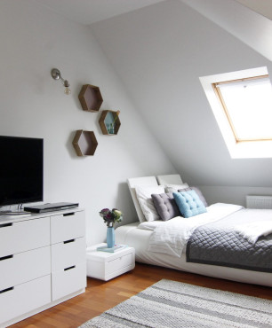 Sypialnia na poddaszu z telewizorem stojącym na białej komodzie