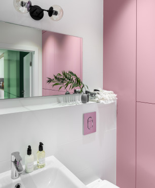 Łazienka z różowym kolorem na ścianie oraz z prostokątnym lustrem z kinkietem