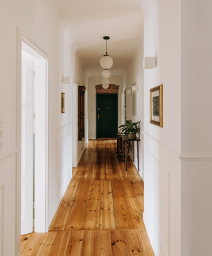 Długi korytarz z drewnianą podłogą  oraz sztukaterią na białej ścianie