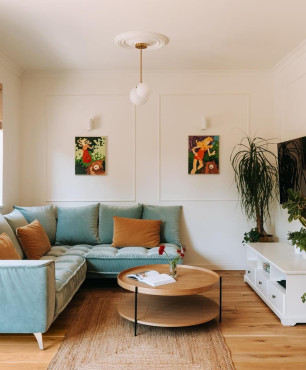 Salon z narożnikiem w kolorze błękitnym, sztukaterią i telewizorem na ścianie  oraz bambusowym dywanem