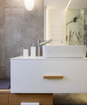Łazienka z szarymi płytkami na ścianie oraz biało-drewnianą szafką z umywalką nablatową